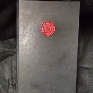 A smooth black leather book with black velvet bookmark and an ornate red wax seal on the cover, sitting on a crinkled black background.